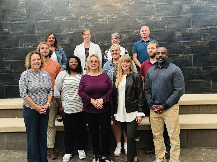Group of 11 people posing in front of wall