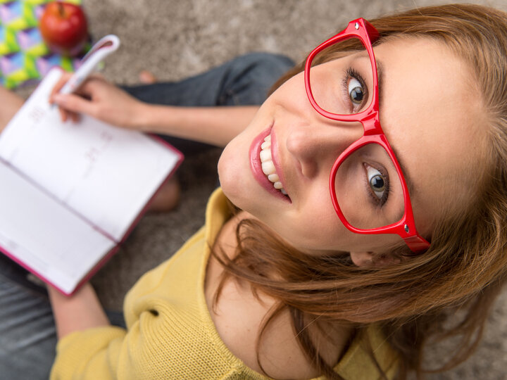 student with red glasses looking up from book